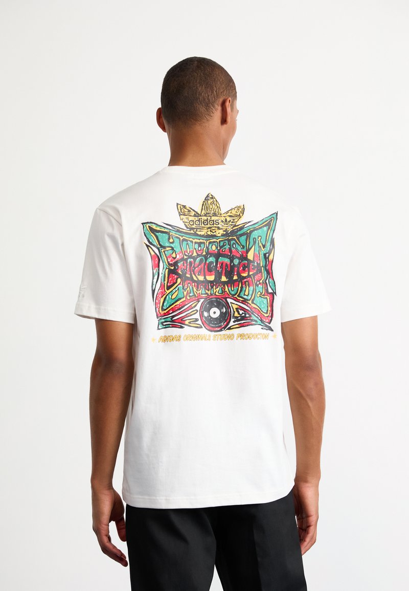 Vit bomullströja med en färgglad grafisk design på baksidan som har en ögonmotiv och texten "Adidas Originals Studio Production".