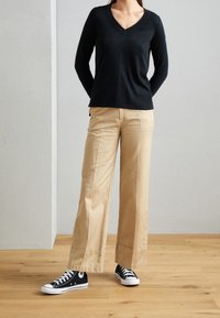 Svart v-halsad tröja, beige vida byxor och svarta canvas sneakers med vita sulor. Minimalistisk design och avslappnad passform.