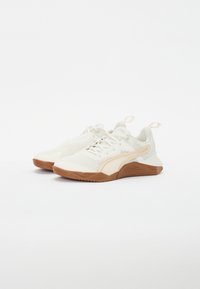 Scarpe atletiche bianche con tomaia in rete testurizzata, dettagli beige e suola in gomma marrone. Presentano un colletto imbottito e un design con lacci.