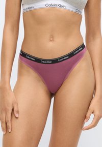 Γυναικείο εσώρουχο τύπου στρινγκ Calvin Klein σε μωβ απόχρωση, με μαύρη μέση που φέρει λευκό λογότυπο. Λείο ύφασμα και μινιμαλιστικός σχεδιασμός.