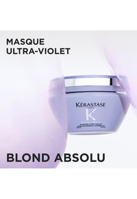 Lila Glas der Kérastase Blond Absolu Ultra-Violet Haarmaske mit silbernem Deckel, zwischen zwei Händen auf weißem Hintergrund gehalten.