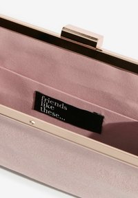 Ružičasti neseser s metalnim okvirom, unutarnjom postavom u svjetlijoj ružičastoj boji i crnom tkaninom oznakom na kojoj piše "prijatelji kao ovi..."