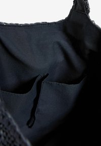 Interiér černé tkané tašky na rameno s hladkou látkovou podšívkou, dvěma kapsami a stahovací šňůrkou uprostřed.