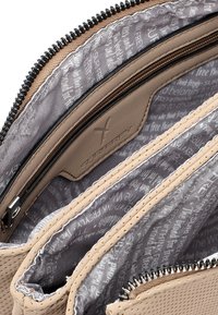 Interno della borsa color tan con più scomparti; pelle liscia, chiusura con zip e una fodera grigia a motivo con dettagli testuali.