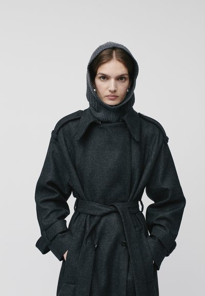 Cappotto di lana grigio scuro con vita cinturata, dettagli a bottoni e colletto alto dotato di cappuccio in maglia. Tessuto spesso e testurizzato.