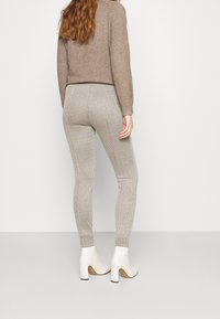 Beiger Pullover kombiniert mit strukturierten, karierten beigen Leggings und weißen Absatzstiefeln. Das Outfit zeichnet sich durch eine figurbetonte Silhouette und neutrale Farbtöne aus.