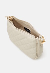 Beige gesteppte Handtasche mit goldfarbenen Beschlägen und einem Reißverschluss. Innenfutter aus Stoff; mit einem Logotag. Abgerundete Form, glatte Textur.