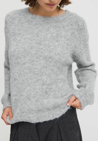 Pull en tricot gris avec une finition douce et texturée, présentant un col rond et des manches longues, tombant délicatement en bas.
