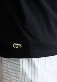 T-shirt en coton noir avec un logo de crocodile brodé vert sur l'ourlet, associé à un short à rayures verticales blanches.