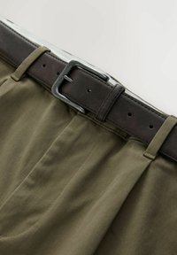 Olive green cotton trousers with a brown leather belt. The belt features a silver metal buckle and loop, with stitched detailing on the fabric.