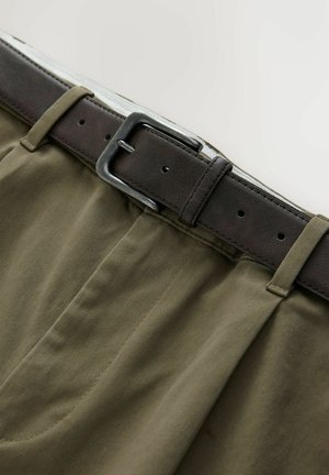 Pantaloni in cotone verde oliva con una cintura in pelle marrone. La cintura presenta una fibbia e un anello in metallo argentato, con dettagli cuciti sul tessuto.