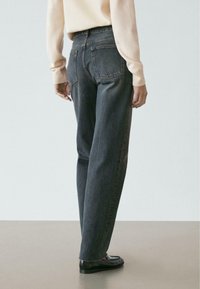 Jeans grigi scuro a vita alta con taglio dritto. Presentano tasche posteriori e cuciture discrete. Indossati con una maglietta chiara e scarpe nere.