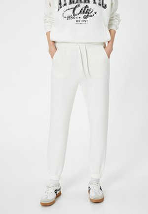 White jogger pants made of soft fabric, featuring an elastic waistband with drawstring, tapered ankle cuffs, and side pockets.