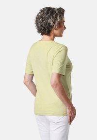 Hellgrünes T-Shirt mit kurzen Ärmeln aus weichem Stoff, mit rundem Halsausschnitt und lockerer Passform, von hinten gezeigt mit weißen Hosen.