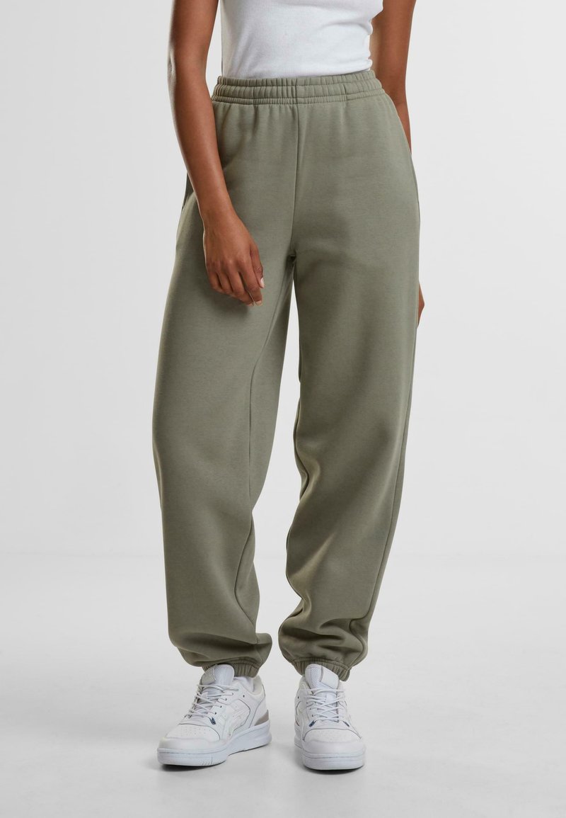 Grønne joggebukser med løs passform laget av myk stoff, med elastisk linning og mansjetterte ankler, stylet med hvite joggesko.
