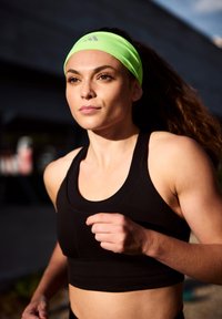 Schwarzes sportliches Crop-Top mit sleekem Design. Ein leuchtend neongrüner Stirnband mit Logo. Das Motiv ist in Bewegung, was Aktivität suggeriert.