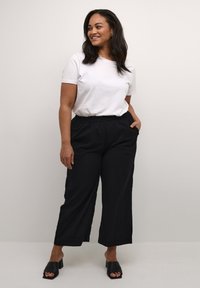 Pantaloni neri a gamba larga con vita elasticizzata e tasche laterali, abbinati a una T-shirt bianca semplice. Il modello indossa tacchi aperti neri.