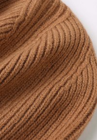 Brown knitted beanie with vertical ribbing texture, made of soft wool. Features a snug fit and a rounded top design.