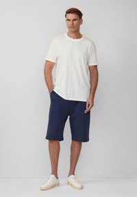 Witte t-shirt met korte mouwen gecombineerd met marineblauwe knielange shorts, gedragen met beige sneakers. Eenvoudig ontwerp en relaxte pasvorm.