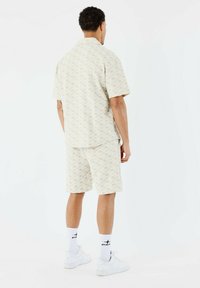 Chemise à col à manches courtes et short assorti en beige clair avec un motif géométrique, en tissu léger. Baskets blanches et chaussettes.