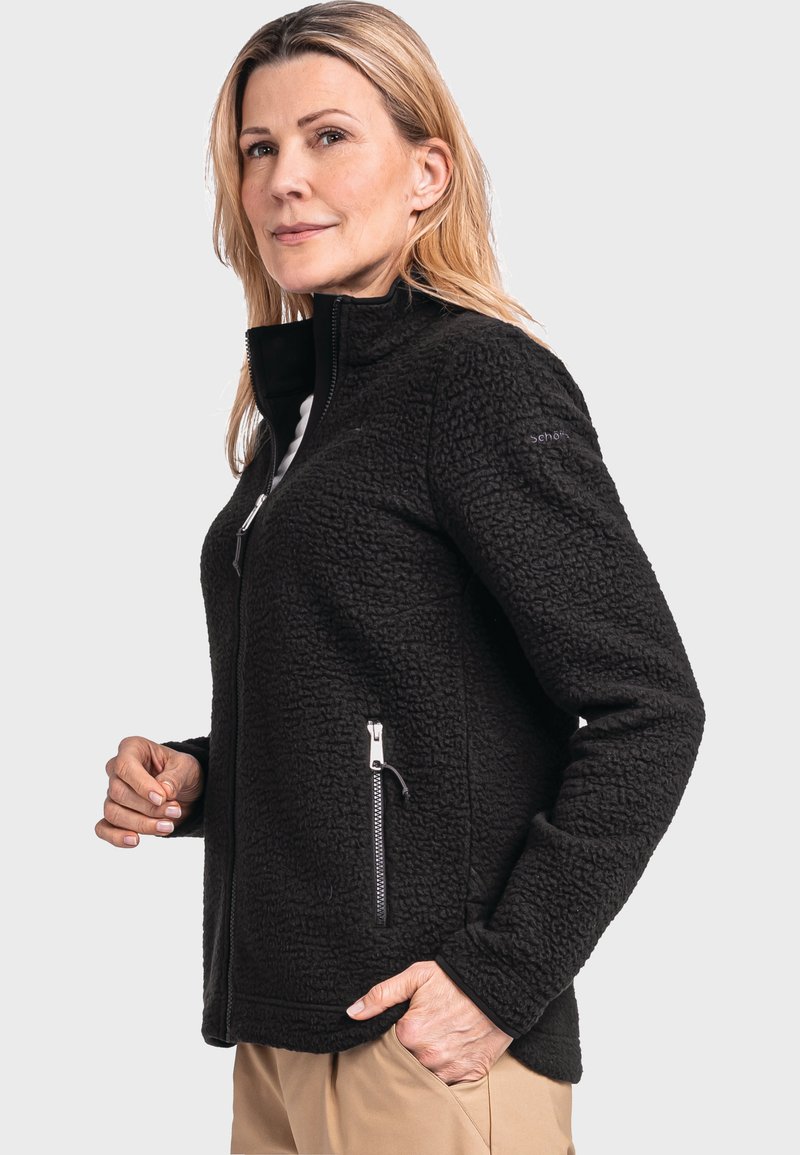 Giacca in pile nera con colletto alto, tasche con zip e superficie testurizzata. Presenta una vestibilità aderente e dettagli delle zip a contrasto.