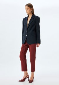 Navy blazer with sharp lapels and two silver buttons, paired with fitted burgundy pants and glossy red high-heeled shoes.