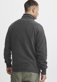 Gray fleece pullover with high collar, raglan sleeves, and ribbed cuffs. Simple design with a small patch on the upper back.