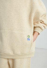 Sweat-shirt beige en tissu texturé, coupe oversize, avec une poche avant. Présente un patch logo coloré "House of Colors".