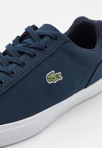 Navy blue canvas sneaker with white sole, navy laces, and a small green crocodile logo on the side.