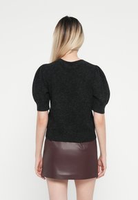 Svart strikket genser med puffede korte ermer, kombinert med et burgunder skinnminiskjørt. Enkelt design, teksturert stoff, og rene linjer.