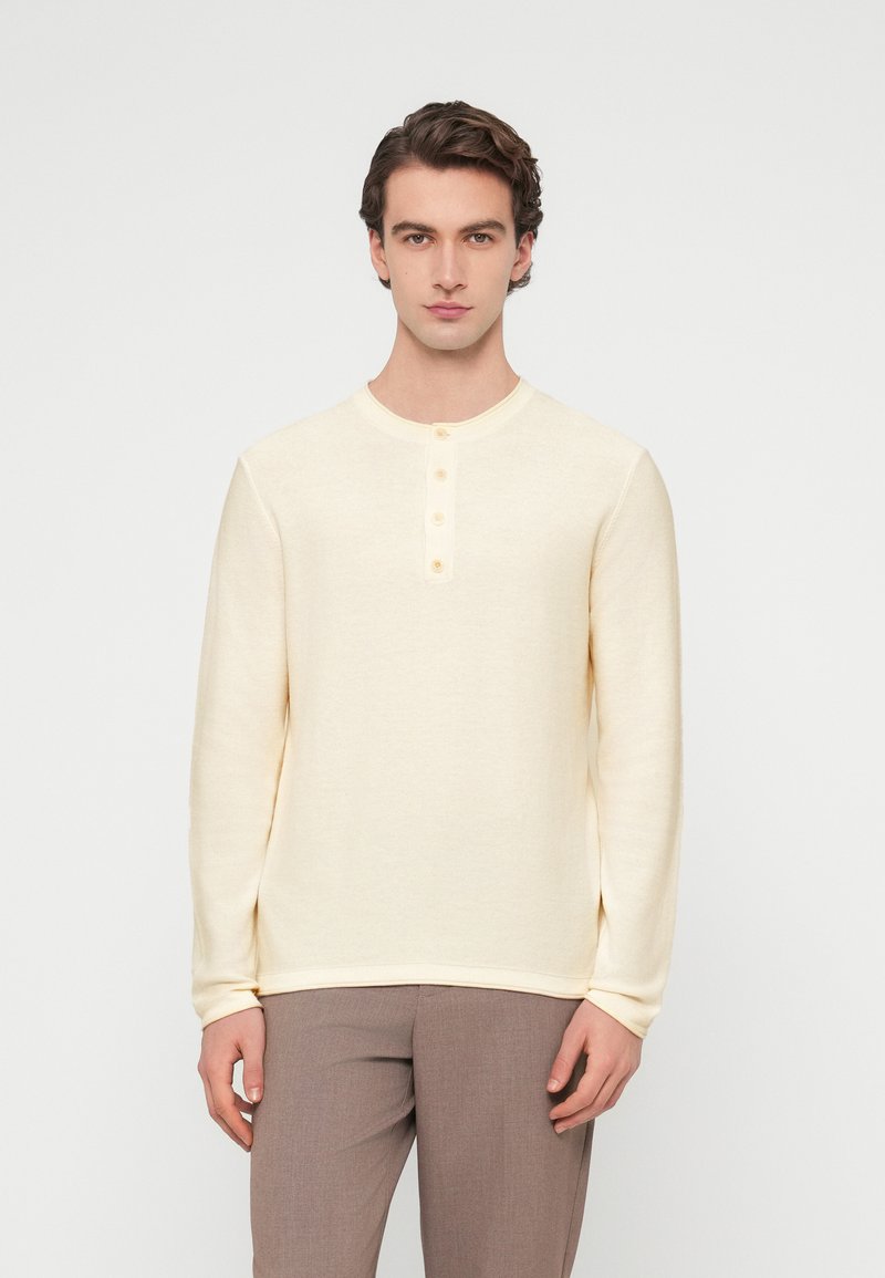 Ανοιχτό κίτρινο πουκάμισο μακρυμάνικο με στρογγυλή λαιμόκοψη, πέντε κουμπιά και απαλό ύφασμα. Συνδυάζεται με ανοιχτό καφέ παντελόνι.