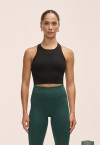 Crop top noir à côtes avec un col haut, associé à un legging vert taille haute, mettant en valeur la texture lisse du tissu et des lignes épurées.