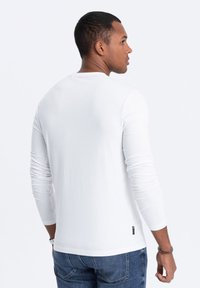 Weißes Langarmshirt aus weichem Stoff, mit Rundhalsausschnitt und schmalem Schnitt. Begleitet von blauen Denim-Jeans mit sichtbaren Nähten.