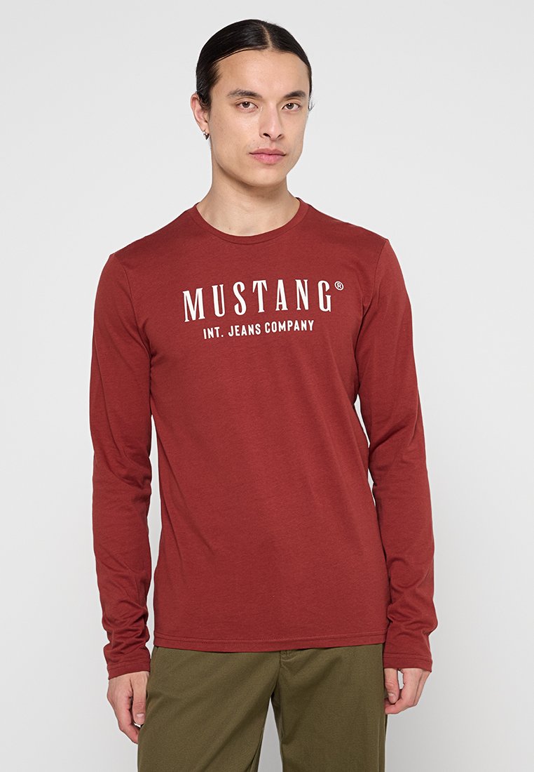 Czerwona koszula z długim rękawem z białym napisem "MUSTANG INT. JEANS COMPANY" na klatce piersiowej; miękka tkanina z okrągłym dekoltem.