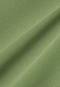 Hellgrüner Stoff mit einer strukturierten, waffelähnlichen Strickmusterung, dargestellt in sanften Falten und gleichmäßiger Beleuchtung.