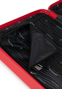 Intérieur de valise rouge avec un compartiment zippé et une poche en maille, avec un revêtement noir arborant un motif d'avion blanc et un nom de marque.