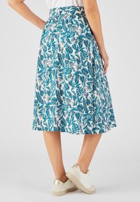 Une jupe mi-longue avec un motif de feuilles teal et blanc, dotée d'une taille élastique et d'un design fluide. Associée à des baskets blanches et dorées.