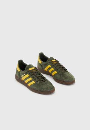 Paar grüne Wildleder Adidas-Sneakers mit gelben Streifen und braunen Sohlen auf hellgrauem Hintergrund.