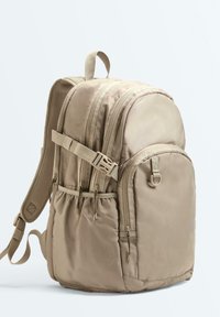 Sac à dos beige en nylon avec plusieurs compartiments zippés, bretelles rembourrées réglables, poches latérales et une anse de transport supérieure.