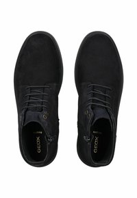 Par de botas de tobillo de ante negro con cordones y cremalleras laterales, punteras redondas y plantillas con marca, vistas desde arriba sobre un fondo blanco.