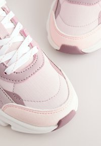 Gros plan de baskets de sport roses et blanches avec des lacets blancs et des détails en tissu texturé sur la pointe et les côtés.