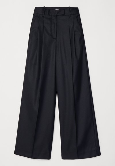 Pantalons noirs à jambes larges en tissu lisse, dotés d'une taille haute, de plis et d'une coupe ajustée. Quincaillerie noire simple à la taille.