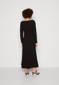 Svart långärmad klänning med en texturerad yta, figurnära byst och utsvängd kjol. Matchad med svarta sandaletter med öppen tå.