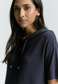 Mørk navy hoodie lavet af blødt stof, med en frontknaplukning, korte ærmer og snoretræk ved hætten.