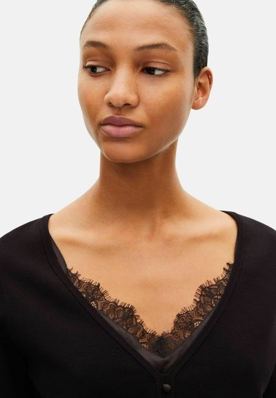 Sort cardigan med V-hals og blonde detaljer ved halsudskæringen. Har en glat struktur og tre små knapper foran.