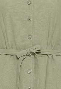 Vêtement vert clair avec cinq boutons sur le devant et une ceinture en tissu nouée en nœud à la taille.