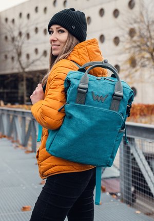 Blue fabric backpack with gray accents and a top handle, featuring a zip closure and front pocket, worn by a person in an orange puffer jacket.