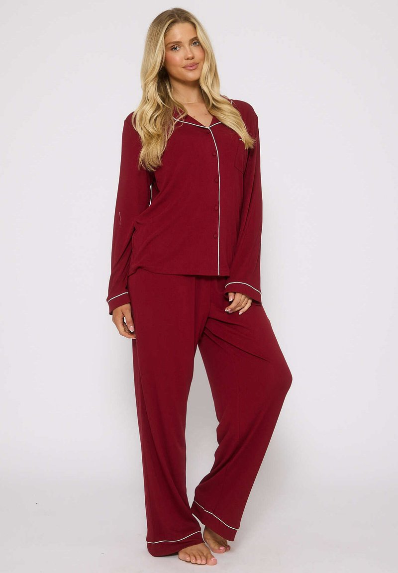 Set di pigiama bordeaux composto da una camicia a maniche lunghe con bottoni e piping bianco, abbinata a pantaloni larghi e comodi. Tessuto morbido.