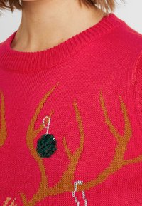 Heldere roze gebreide trui met bruine hoorns en een groene met pailletten versiering, voorzien van een geribde ronde halslijn en een textuurstof.