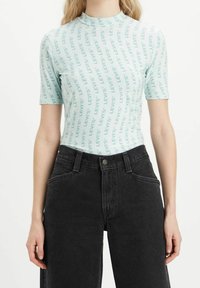 Světle modré obepnuté tričko s opakujícím se vzorem textu "LEVI'S"; spárované s černými džíny s vysokým pasem. Krátký rukáv, hladká textura.